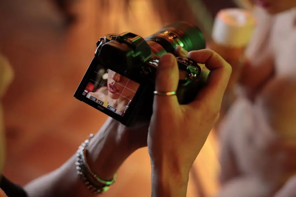 Fotografo cattura un ritratto di una donna visibile solo sul display della fotocamera digitale, evidenziando un'ambientazione soffusa con una sfocatura che suggerisce un contesto sociale o un evento