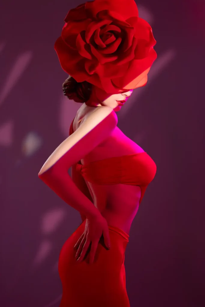 Modella con un grande fiore rosso in testa, indossa un top e una gonna rossa, illuminata con luci rosa e rosse che creano un effetto teatrale e artistico.