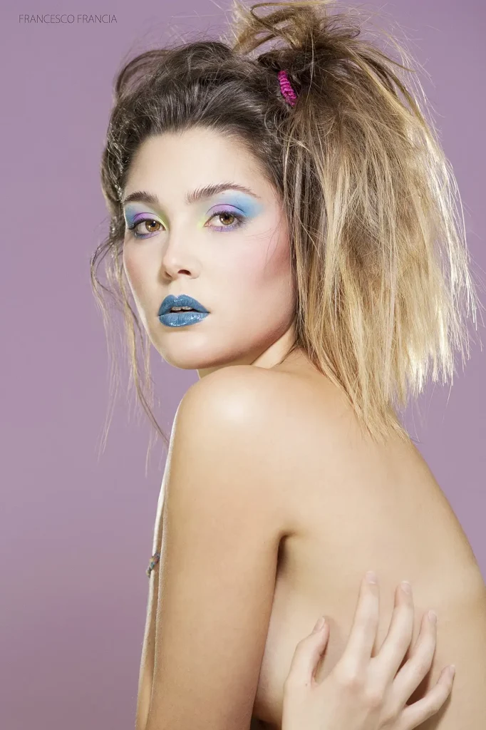 Ritratto di donna con trucco colorato su sfondo viola.