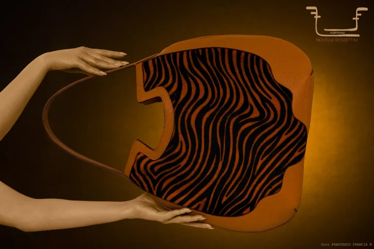Borsa in pelle color cuoio di Novella Rossettini con motivo zebrato interno, tenuta da una mano ocra