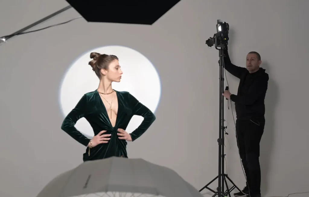 Francesco Francia regola l'illuminazione in studio con una modella in abito verde davanti a uno sfondo illuminato.